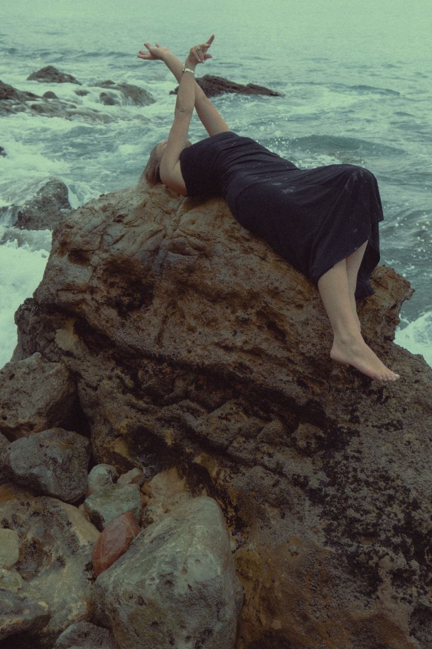 A person resting on a rock as the ocean breaks behind them